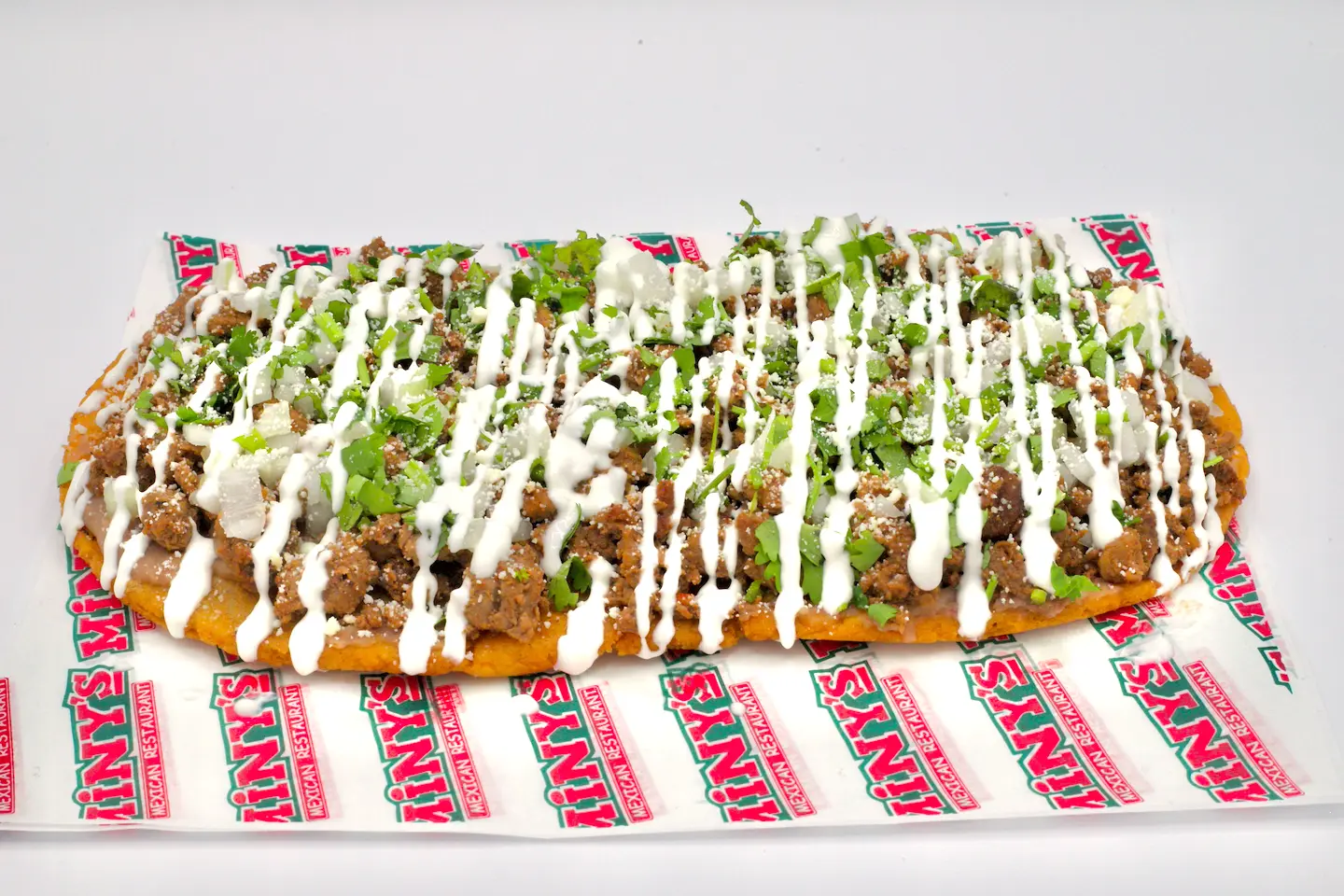 A Miny's huarache topped with meat, crema, cilantro and onion, on red-and-white Miny's paper